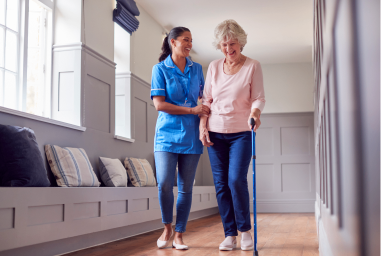 Nurse assisting elderly woman with walking indoors.