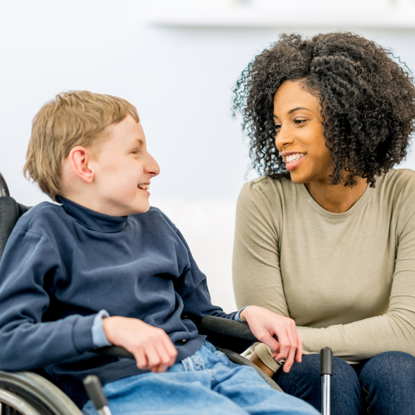 A woman warmly interacting with a boy in a wheelchair.